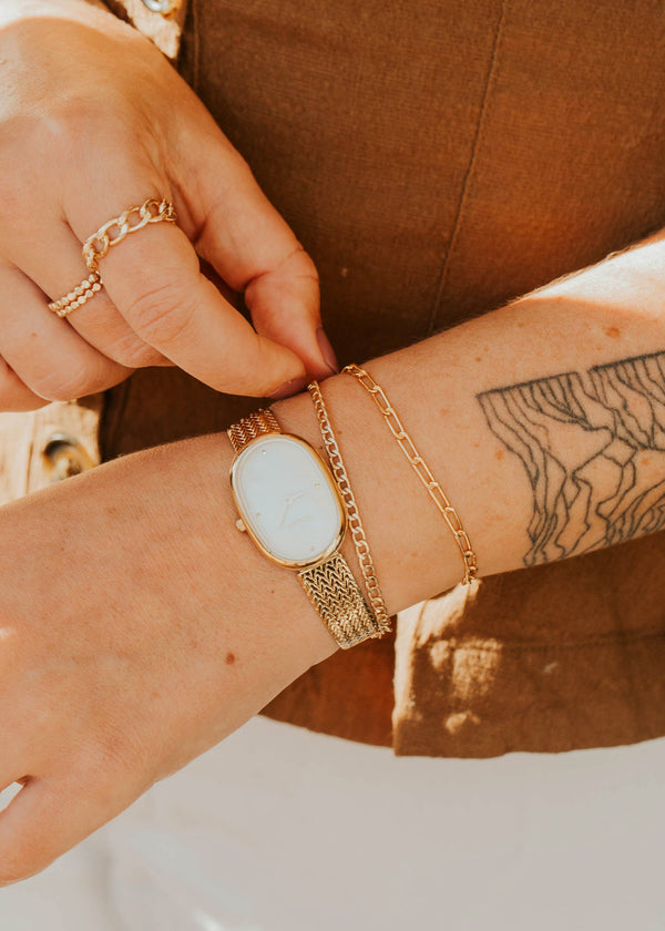 Close-up of a person's wrist with gold bracelet and rings, wearing a brown jacket.