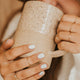 Teeny-Tiny Band by Hello Adorn shown in a ring stack, styled with Beaded Ring, Confetti Ring and Aden Band holding a mug to show the ring stack.