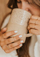 Teeny-Tiny Band by Hello Adorn shown in a ring stack, styled with Beaded Ring, Confetti Ring and Aden Band holding a mug to show the ring stack.