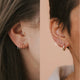 Tiny Twist Earrings shown in an ear in larger size of 8MM and smaller size 6MM paired with a Bold Hoop by Hello Adorn.