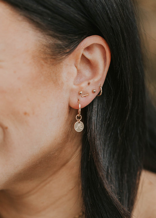 model wearing stud earrings with a charm on a hoop minimal style piercings