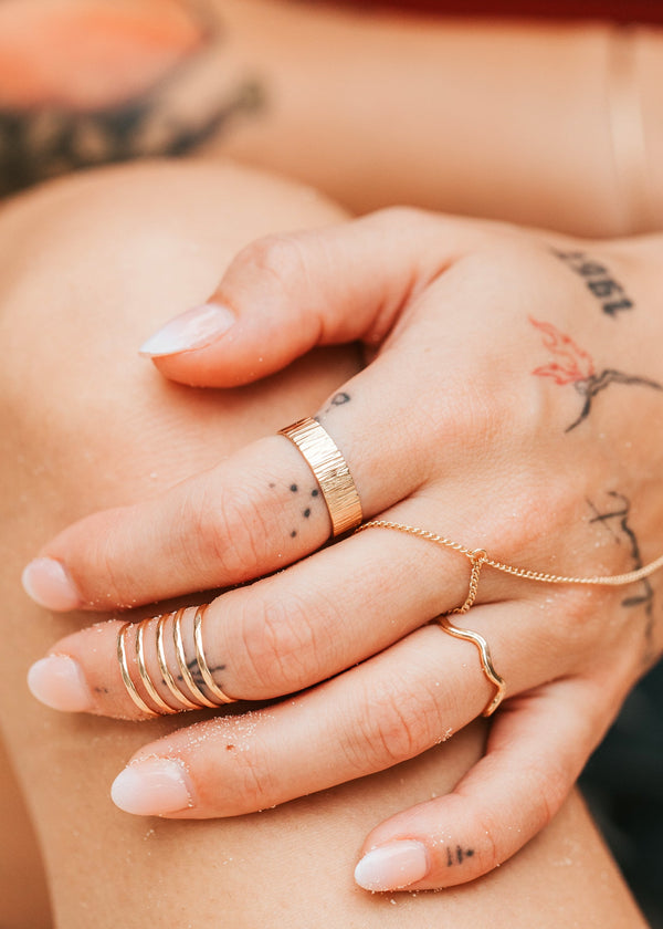 Close-up of a hand with gold rings and tattoos on a blurred background