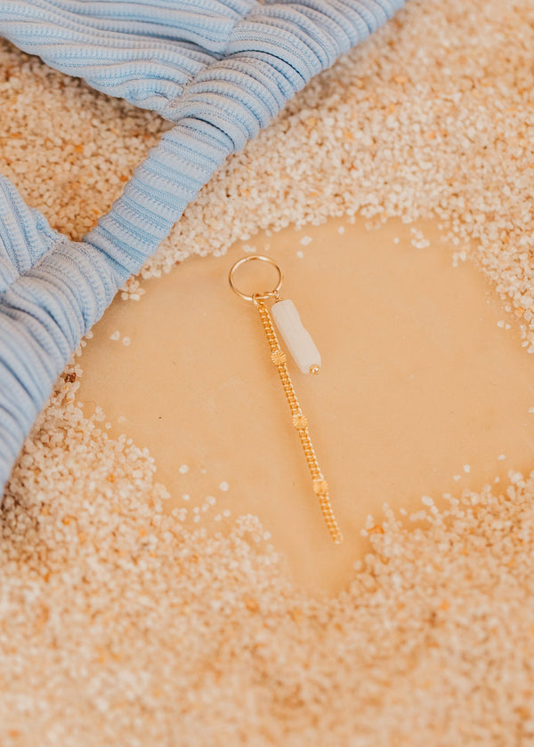 Gold hello adorn bikini charm with a white stone on a textured surface