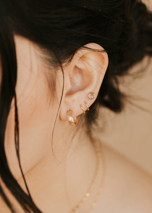 Close-up of an ear wearing gold earrings with a blurred background