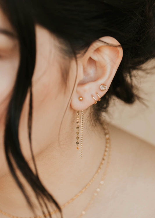 Close-up of an ear with gold earrings and necklaces against a blurred background