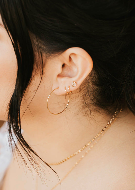 Close-up of a person wearing gold hoop earrings and a delicate necklace.