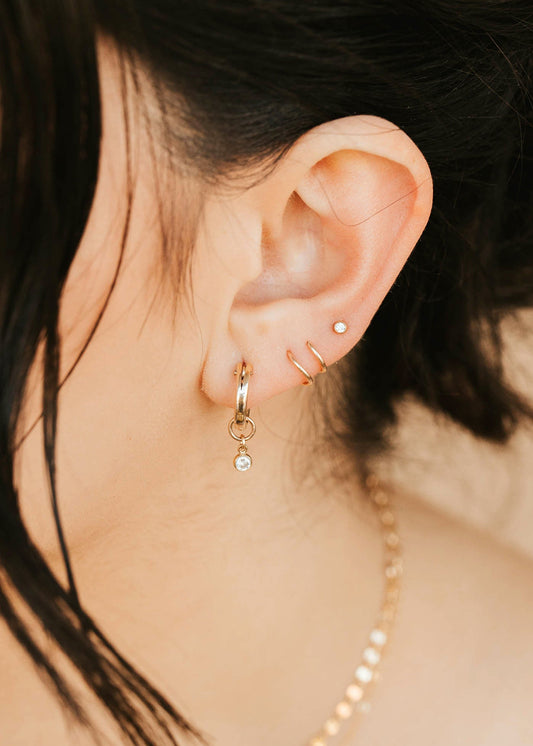 Close-up of an ear with gold hoop earrings and a necklace, with blurred background