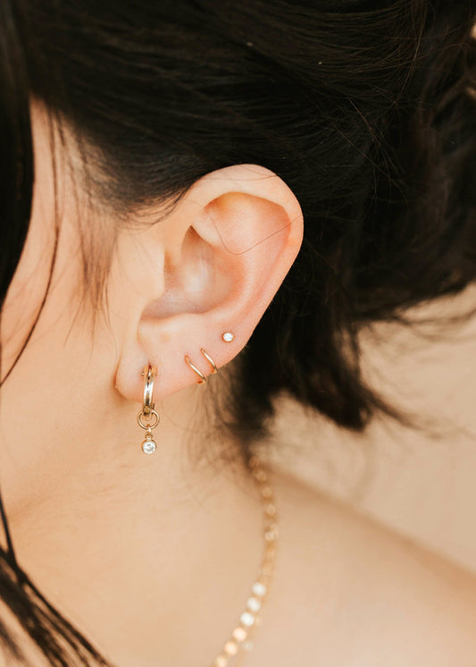Close-up of an ear with gold hoop earrings and a necklace, with blurred background