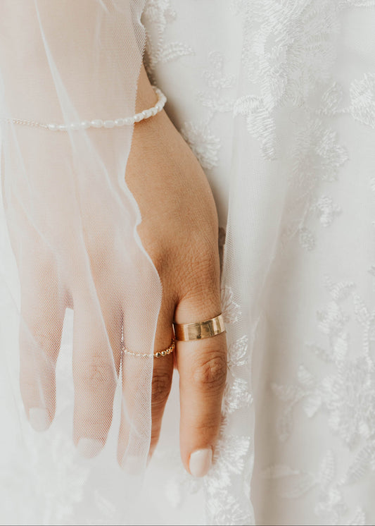 Hand wearing a gold ring with a white lace background