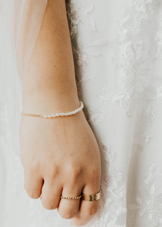 Hand wearing a gold ring with a white lace background