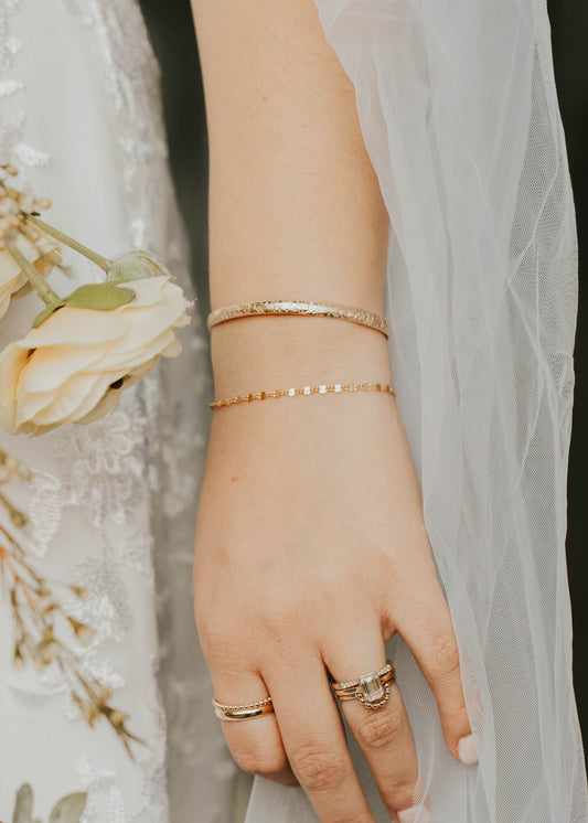 Close-up of a hand wearing rings with a blurred floral background