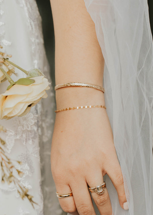 Close-up of a hand wearing rings with a blurred floral background
