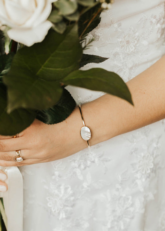 Close-up of a hand holding a bouquet with a wedding dress and bracelet in the background