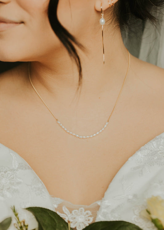 Close-up of a person wearing a delicate necklace and earrings, holding white flowers.