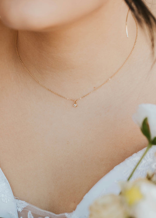 Close-up of a person wearing a delicate gold necklace with a small pendant, holding flowers.