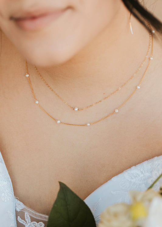 Close-up of a person wearing a delicate gold necklace with a blurred background