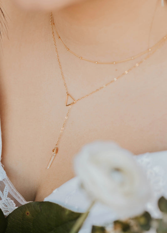 Close-up of a person wearing a gold necklace with a triangle pendant, holding white flowers.