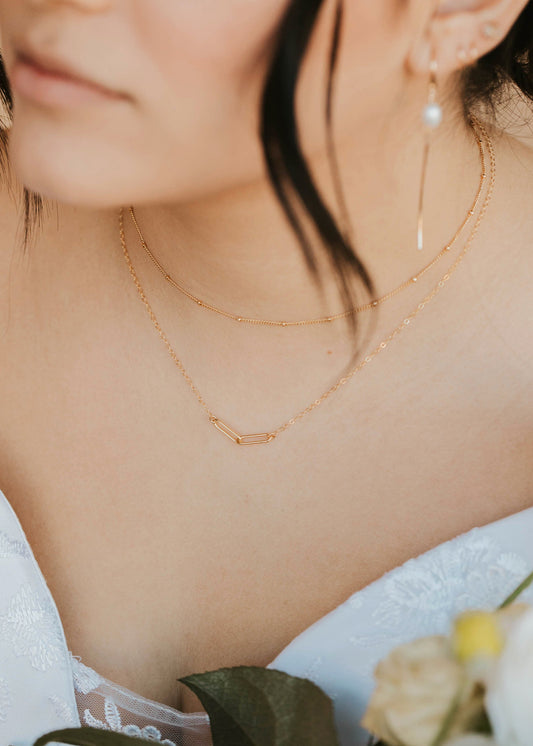 Close-up of a person wearing gold necklaces and earrings with a blurred background