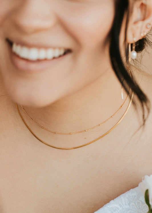 Close-up of a person wearing gold necklaces and earrings, holding flowers.