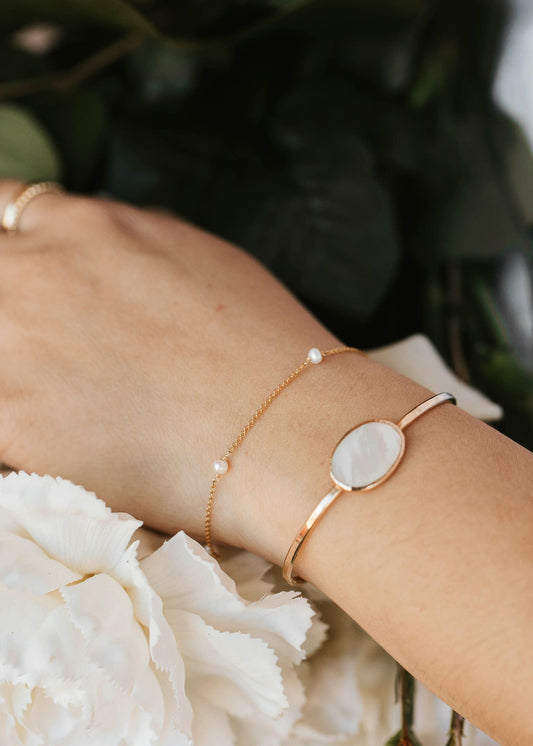 Close-up of a hand wearing a gold bracelet with a stone on a floral background