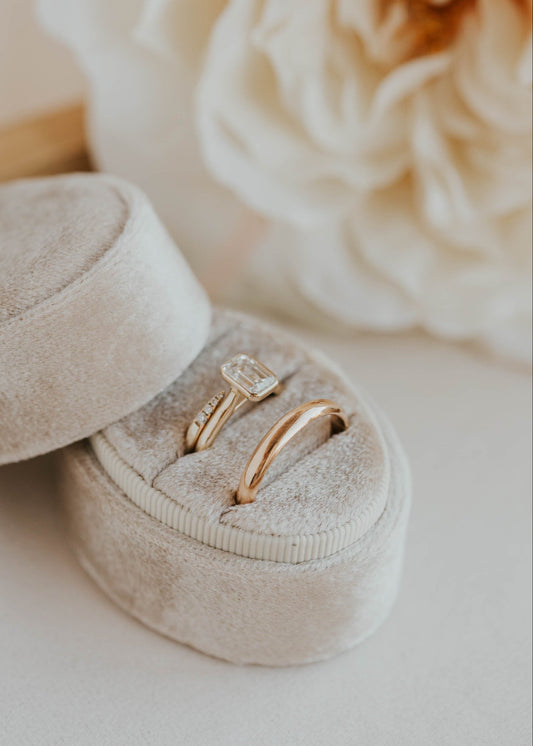 Gold ring in an open beige velvet ring box with a blurred flower in the background