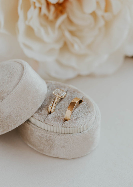 Gold ring in a beige ring box with a white flower in the background