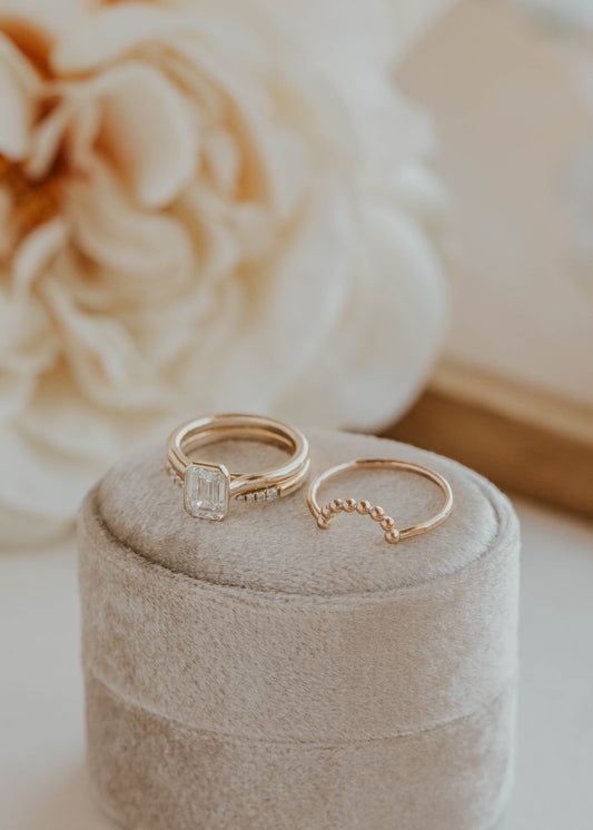 Two gold rings on a beige ring box with flowers in the background