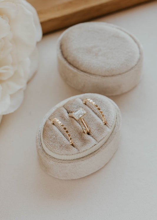 Gold rings in a small round beige velvet box on a light surface with flowers in the background