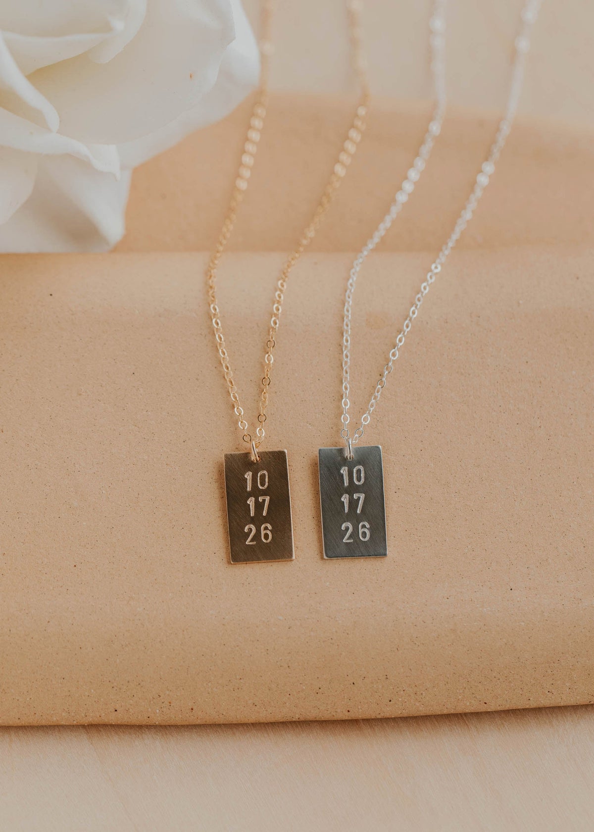 Two necklaces with rectangular pendants on a beige fabric background