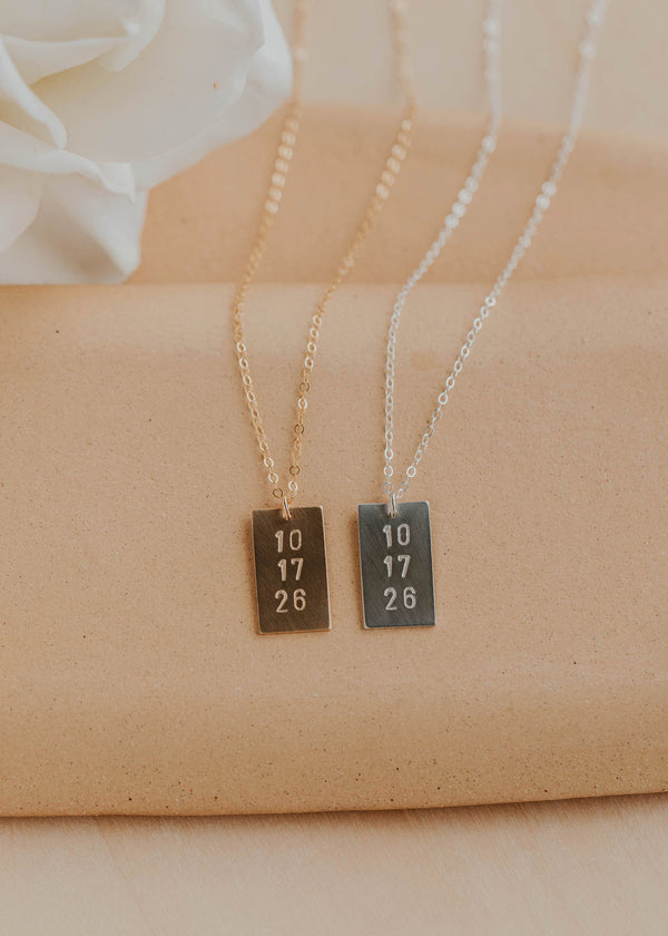 Two necklaces with rectangular pendants on a beige fabric background