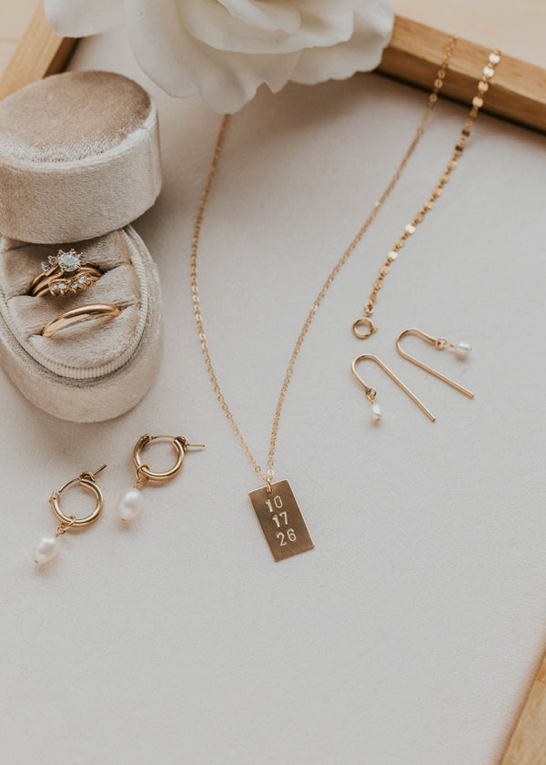 Gold jewelry including a necklace, earrings, and rings on a light surface with a white flower.