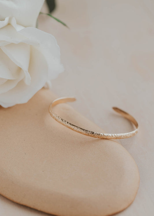 Gold bracelet on a beige surface with a white flower in the background