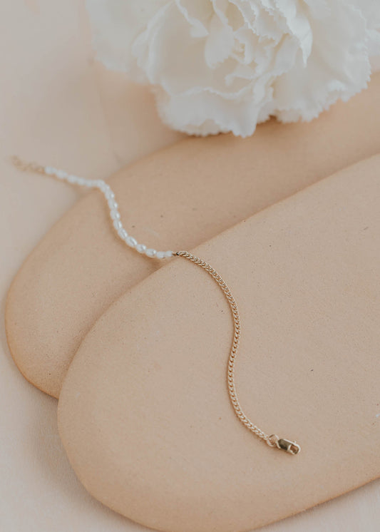 Gold bracelet on a person's wrist with a white flower in the background