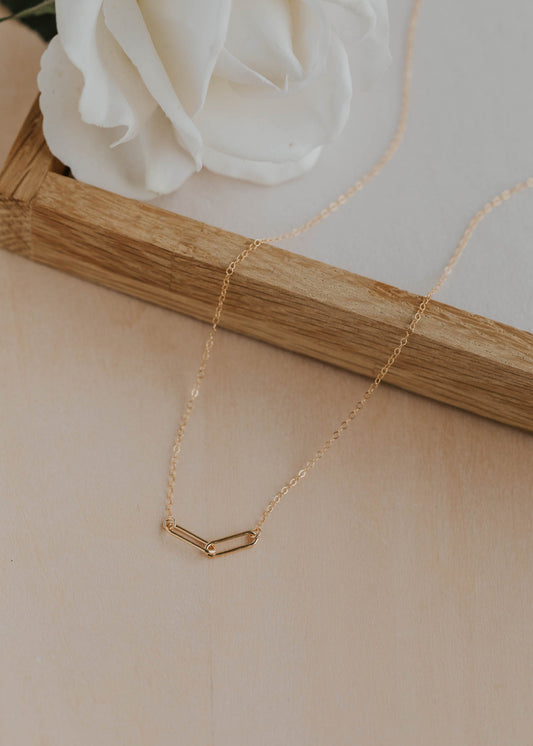Gold necklace on a wooden stand with a white rose in the background
