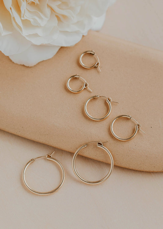 Gold hoop earrings on a beige surface with a white flower in the background