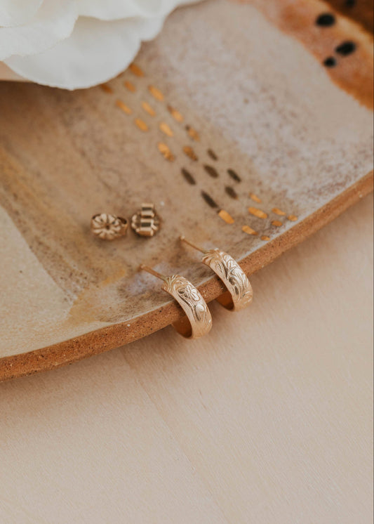 Gold earrings on a textured beige surface with white flowers in the background