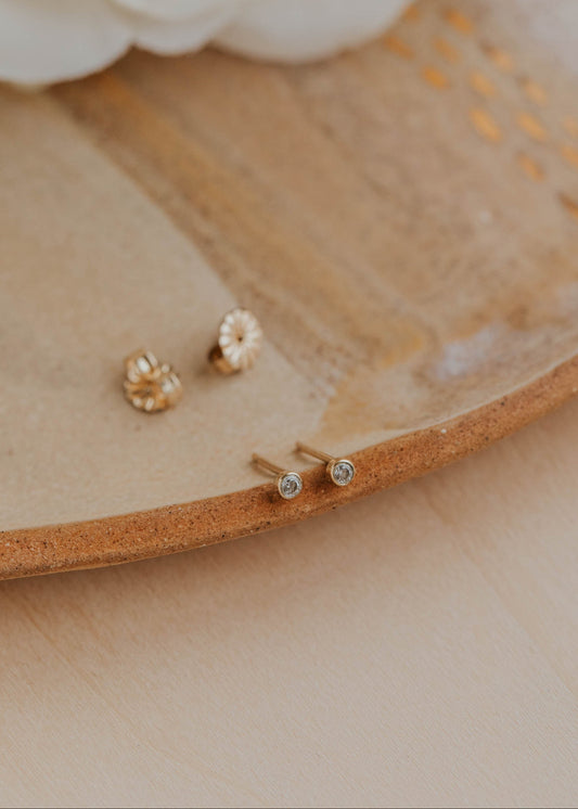 Gold and silver earrings on a wooden surface with white flowers in the background