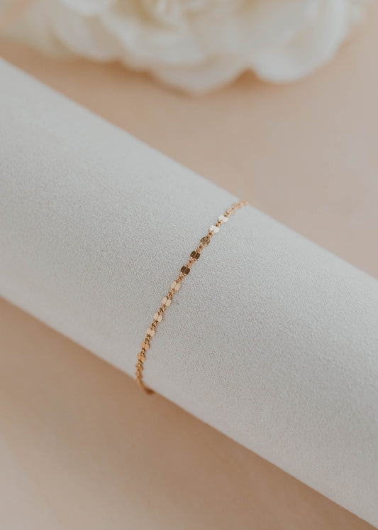 Gold bracelet on a white fabric with a beige flower in the background