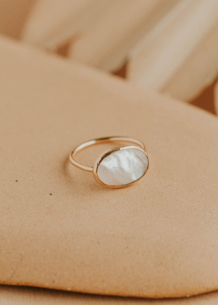 Gold ring with a white stone on a beige surface