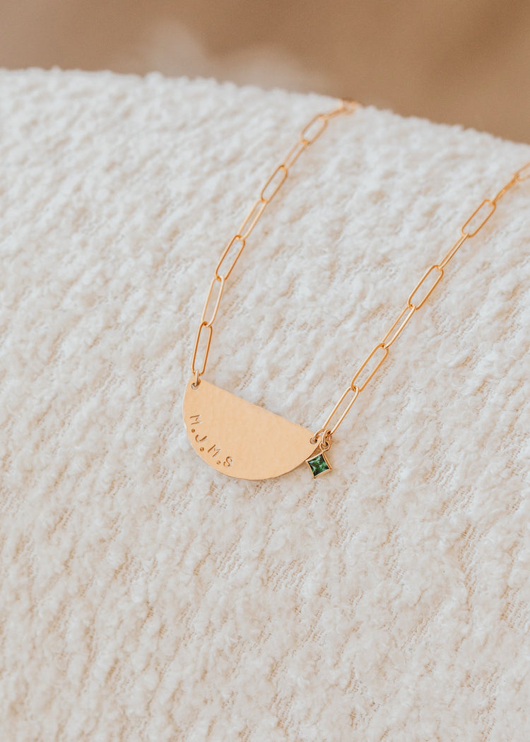 Gold necklace with a green gemstone on a textured beige surface