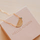 Gold necklace with a half-circle pendant on a 'HELLO ADORN' box.