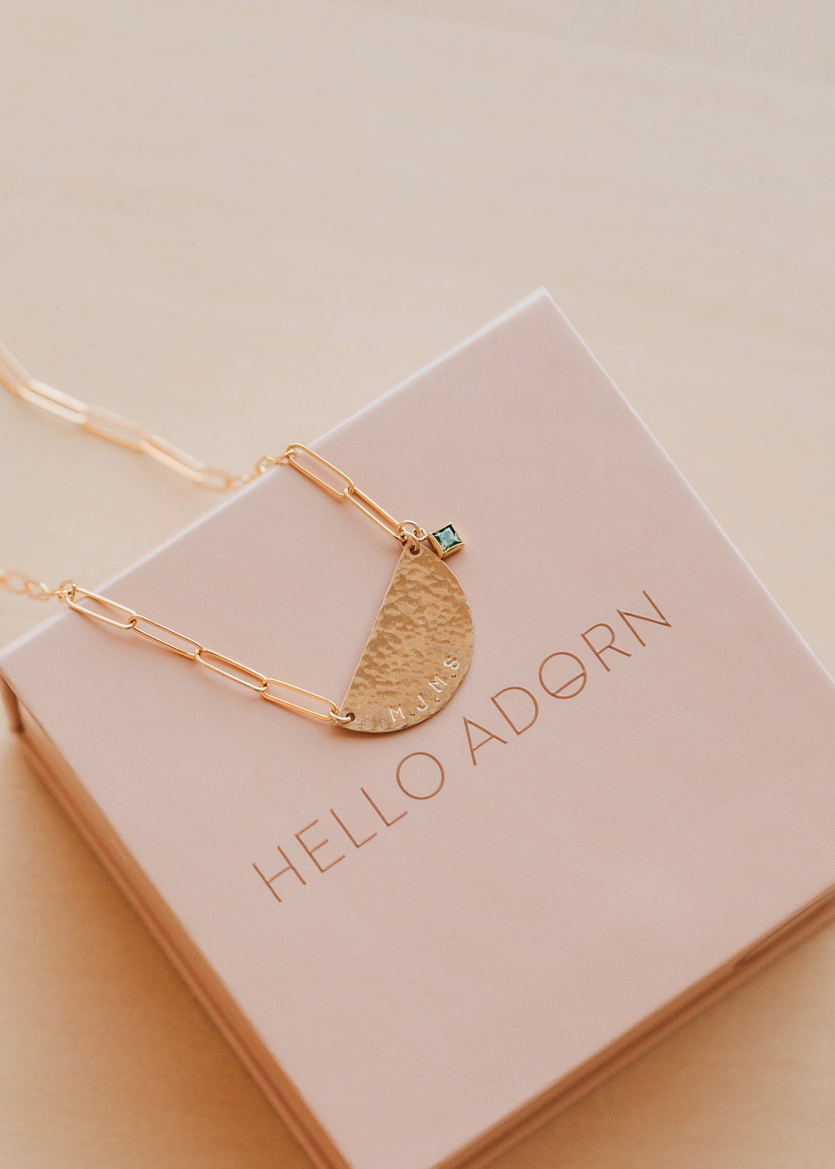 Gold necklace with a half-circle pendant on a 'HELLO ADORN' box.