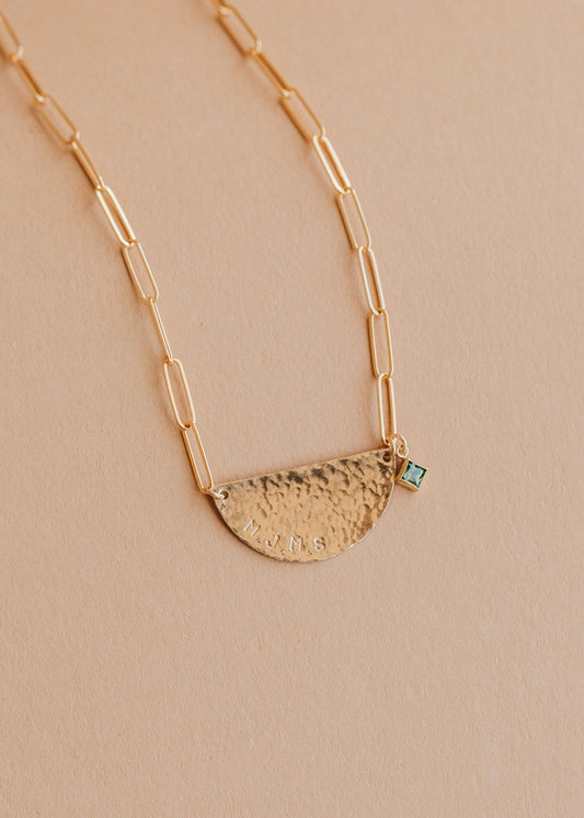 Gold necklace with a half-circle pendant on a beige background
