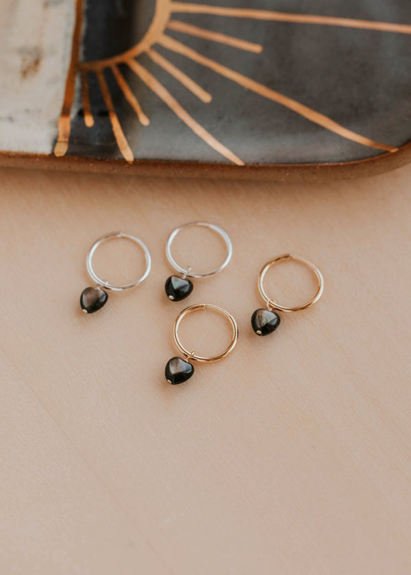 Gold and silver hoop earrings with black stones on a beige surface.