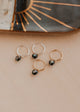 Gold and silver hoop earrings with black stones on a beige surface.