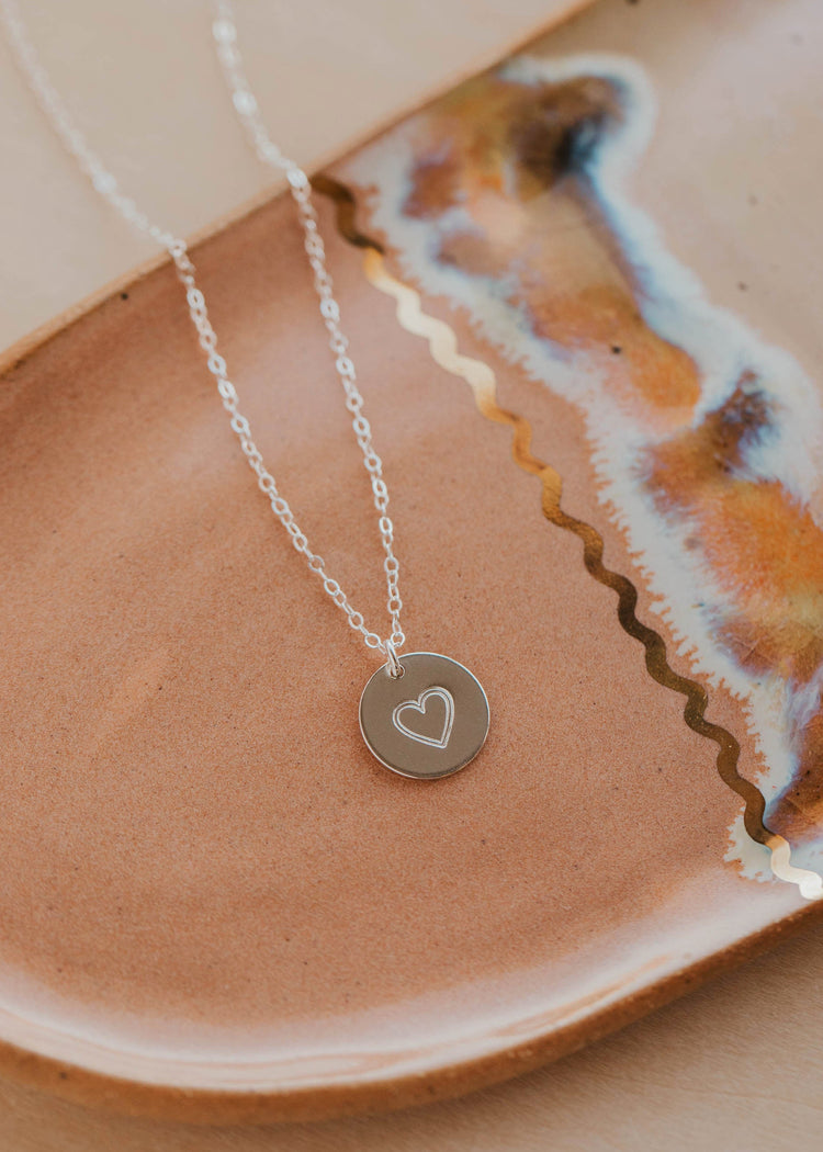 Silver necklace with a heart pendant on a ceramic plate