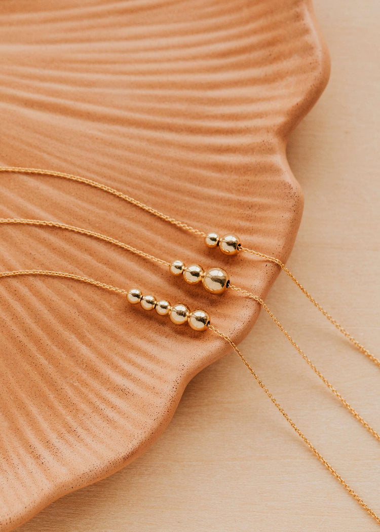 Gold Hello adorn beaded necklaces on a textured beige surface