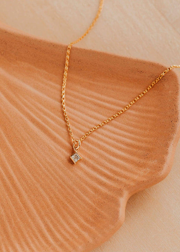 Gold necklace with a diamond pendant on a textured beige surface