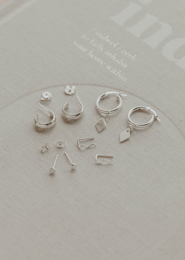 Set of silver earrings on a clear stand with a light gray background