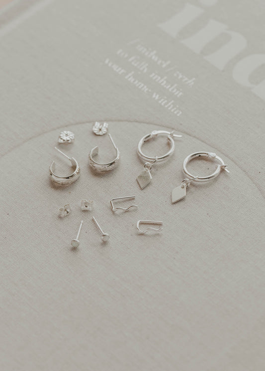 Set of silver earrings on a clear stand with a light gray background